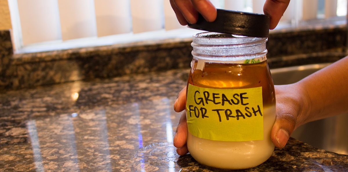 Person putting lid on jar filled with oil and fats with label "GREASE FOR TRASH"
